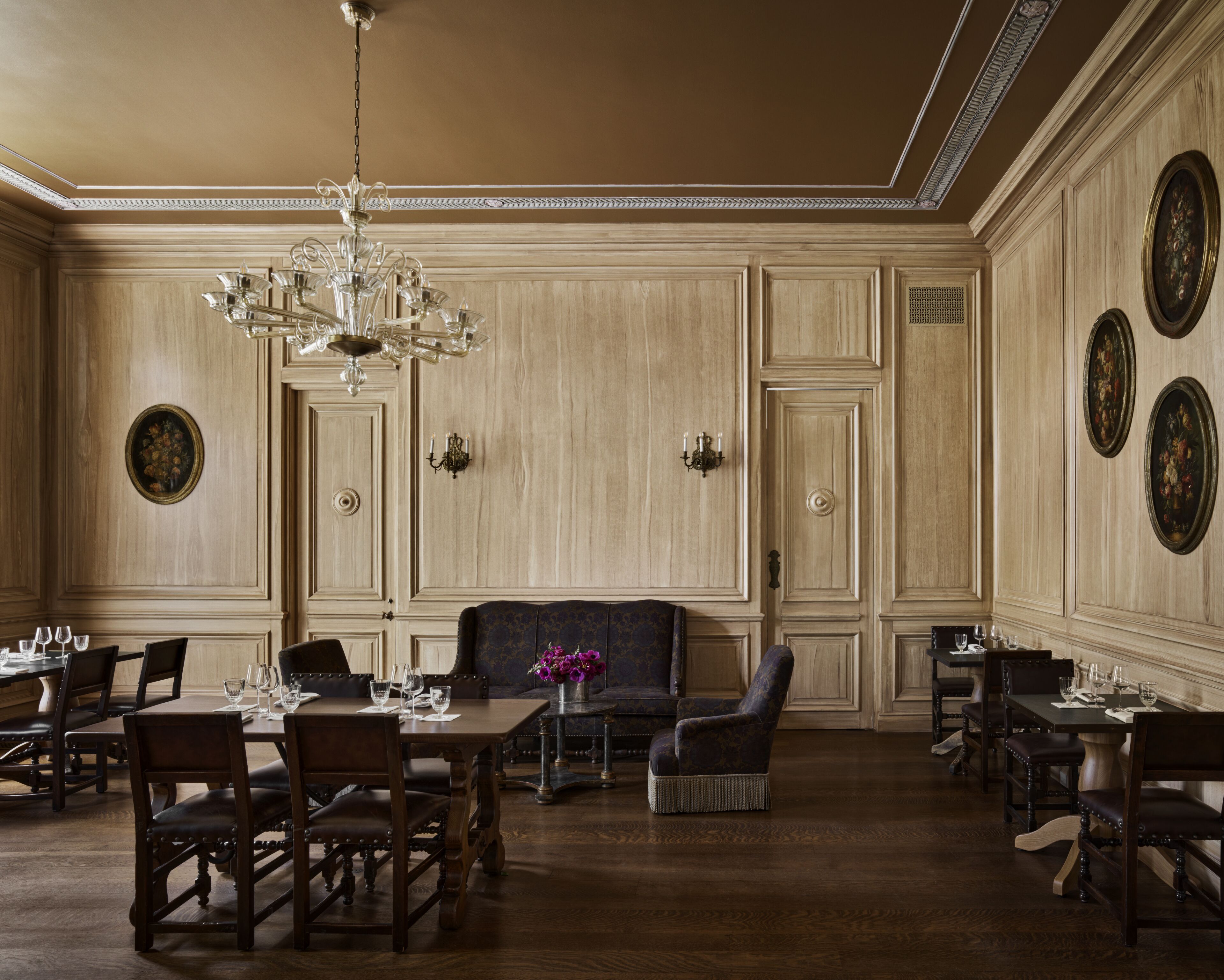 Une salle à manger élégante, avec des boiseries, un lustre et plusieurs tables et chaises.