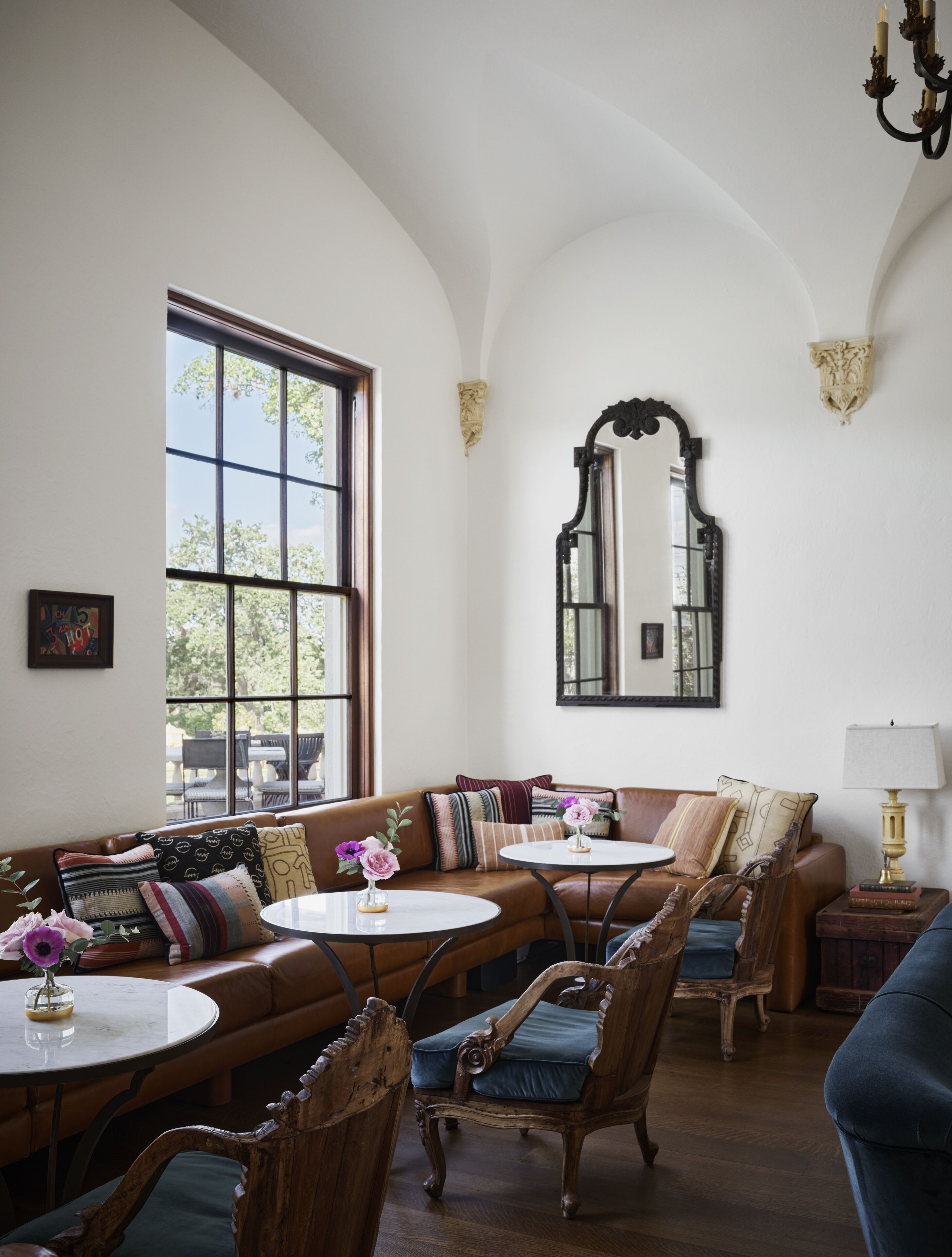 Ein Zimmer mit gewölbter Decke, einem großen Fenster, einem Spiegel, einer Couch, einem Tisch und einem Stuhl.