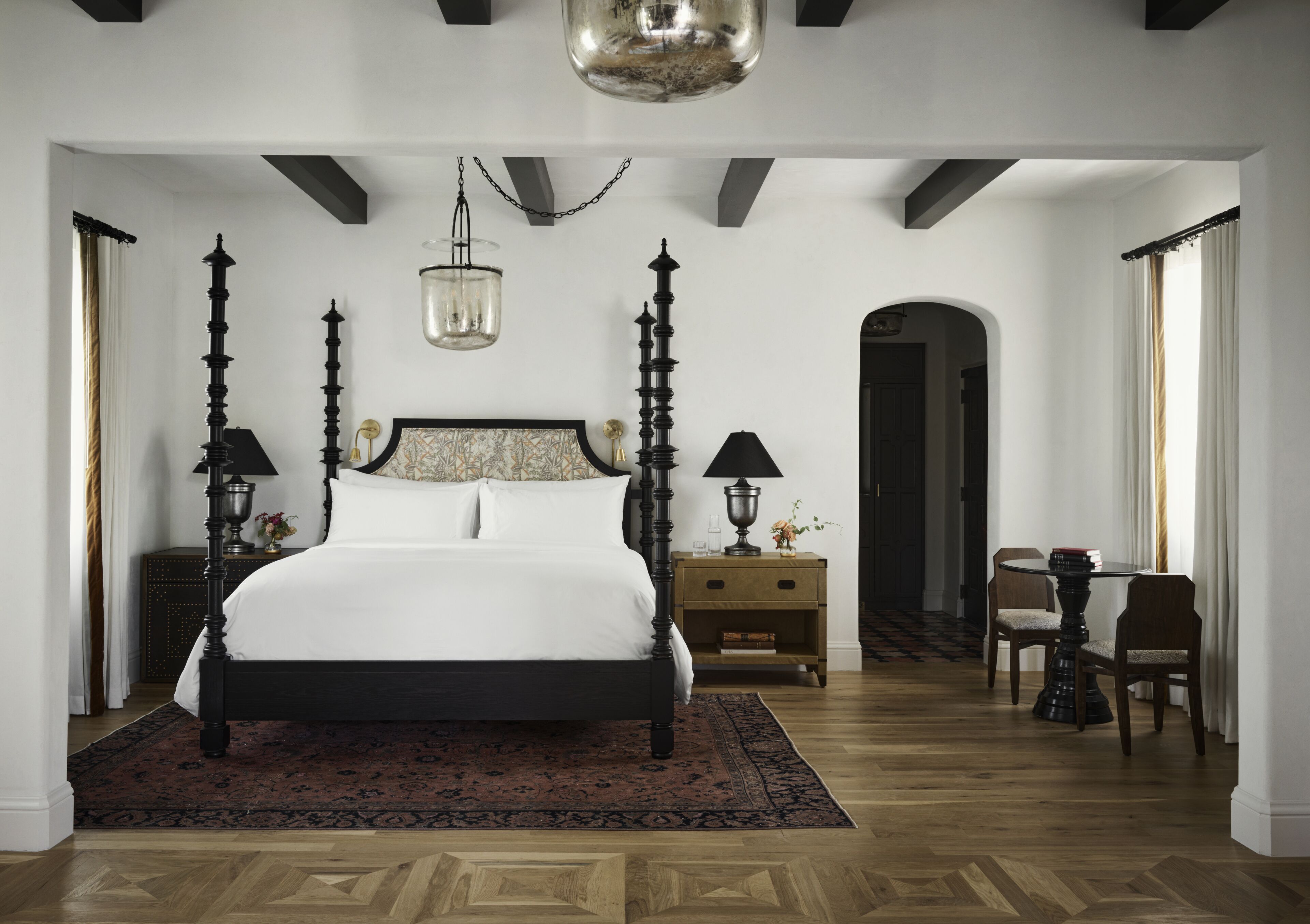 A bedroom with a large bed, two bedside tables with lamps, a small round table with chairs, and a chandelier.