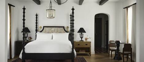 A bedroom with a large bed, two bedside tables with lamps, a small round table with chairs, and a chandelier.