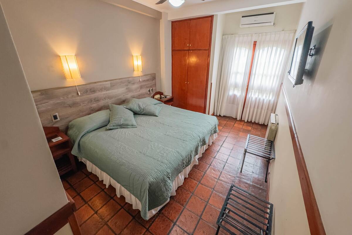 Quarto com cama, abajures, ventoinha no teto, guarda-roupa e janela com cortinas.