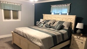 Une chambre à coucher avec un lit, des tables de chevet, un ventilateur et une fenêtre avec des rideaux.