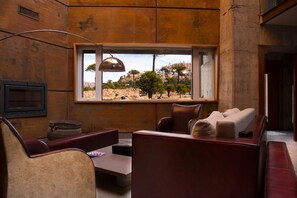 Un intérieur moderne avec des meubles en cuir, une grande fenêtre donnant sur un paysage rocheux et un téléviseur fixé au mur.
