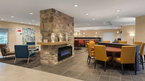 A modern dining area with a stone fireplace, yellow chairs, and a large table. - TownePlace Suites by Marriott Boone (Boone)