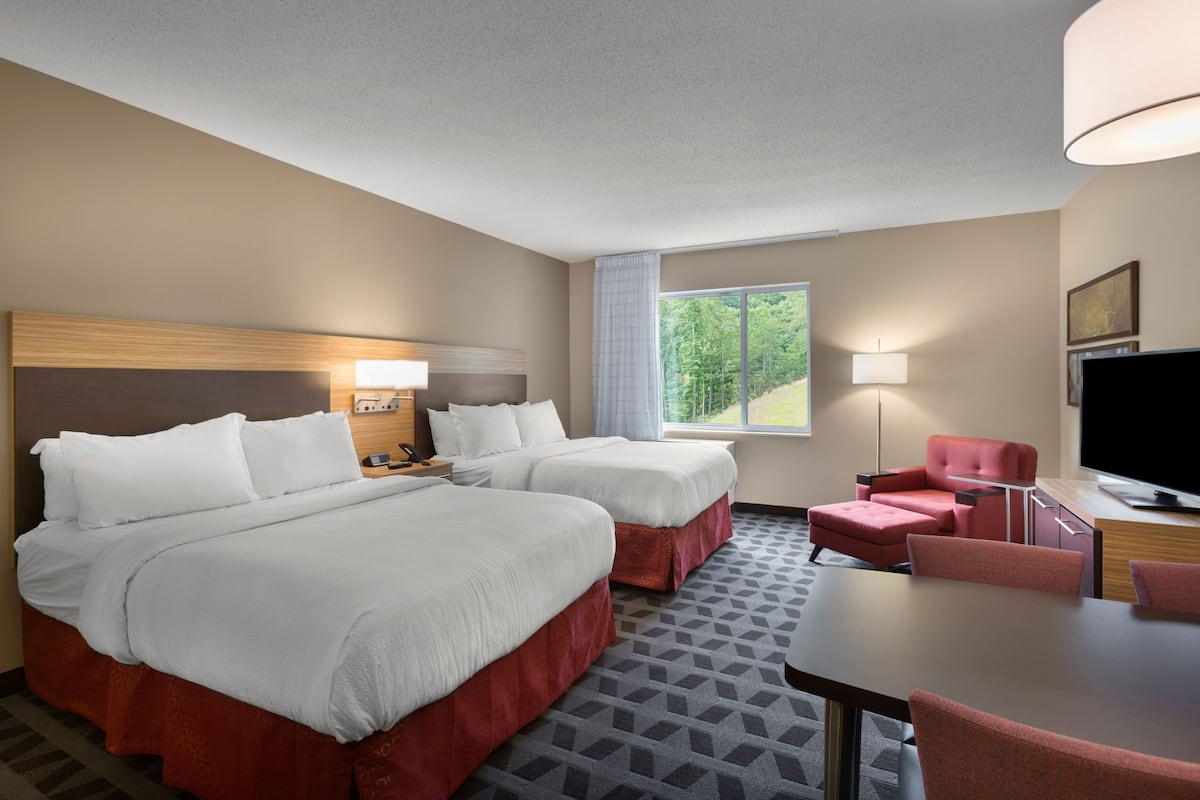 A hotel room with two beds, a desk, a chair, a TV, and a window with a view of trees.