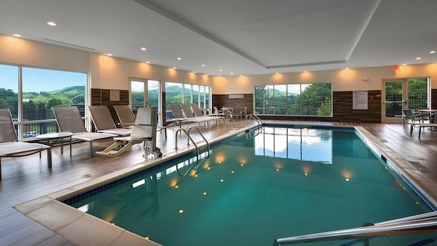 An indoor swimming pool with lounge chairs and tables, large windows, and a view of the outdoors. - TownePlace Suites by Marriott Boone (Boone)