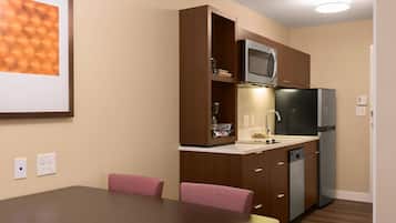 A compact kitchen with a microwave, refrigerator, and built-in dishwasher. There is a dining table with chairs and a wall-mounted light fixture.