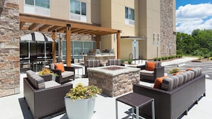 An outdoor patio with wicker furniture, a stone fire pit, and a grill area. - TownePlace Suites by Marriott Boone (Boone)