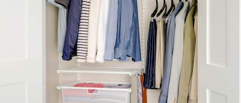 A walk-in closet with hanging clothes, shelves with folded clothes, and a suitcase.