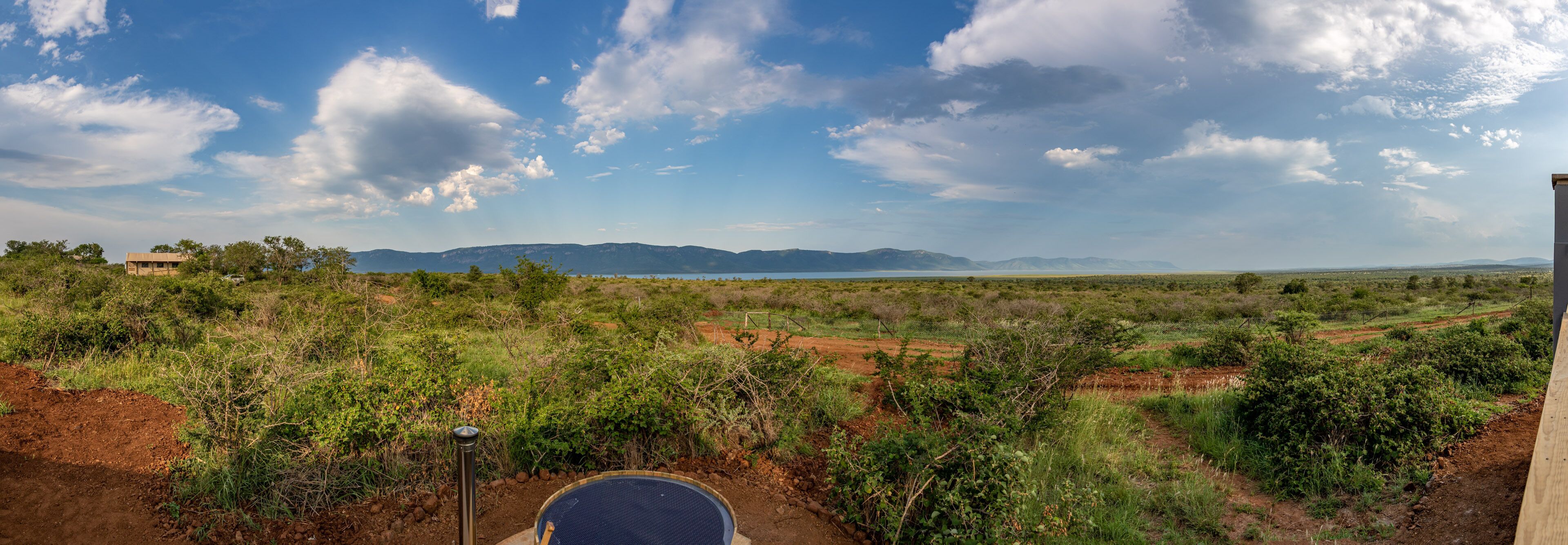 A rural landscape with a dirt path, sparse vegetation, and distant mountains under a partly cloudy sky.