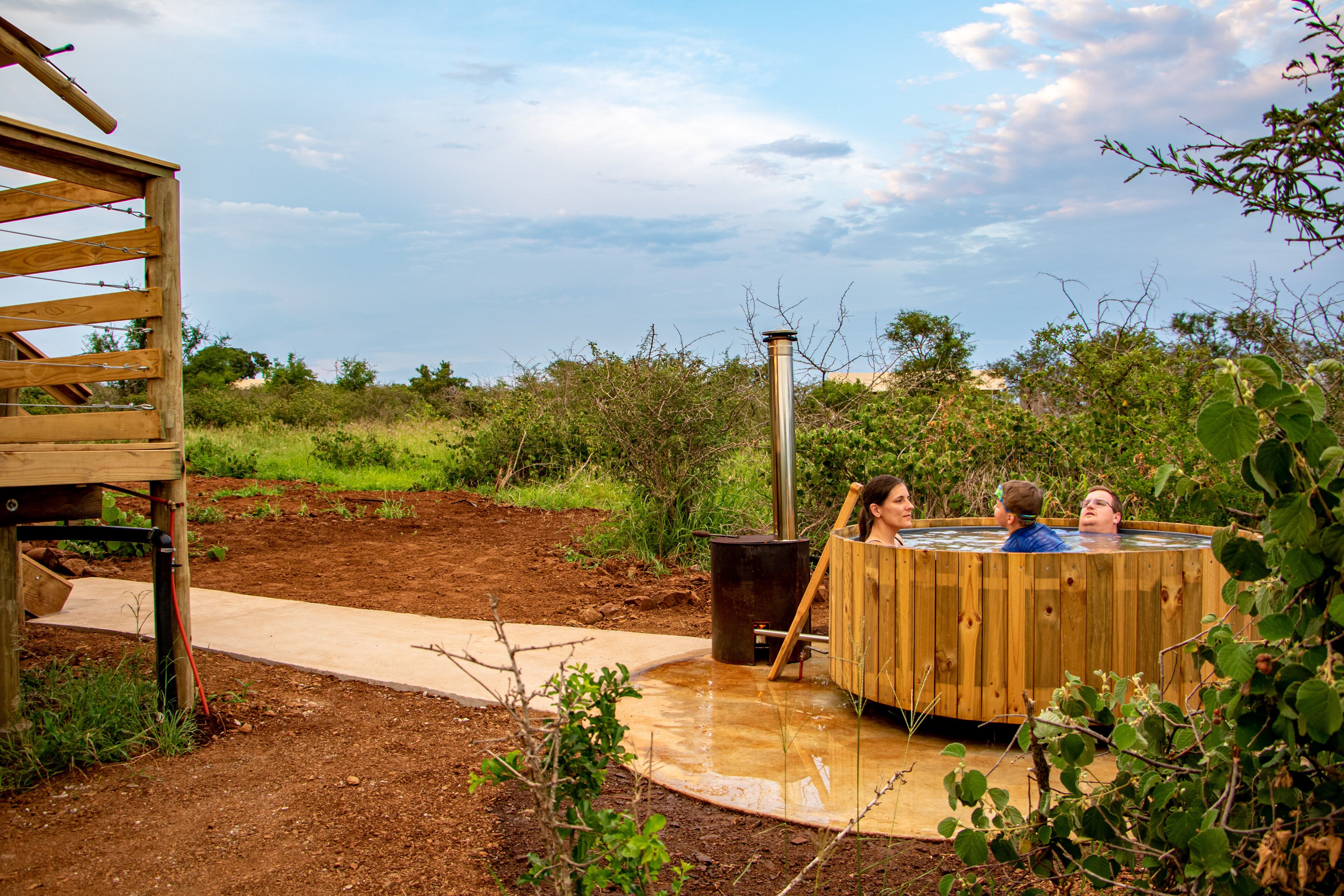 A hot tub in a garden with a wooden deck and a metal chimney.
