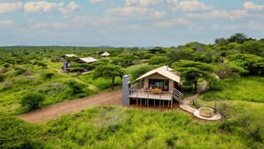A lodge with a deck, surrounded by lush greenery and a dirt path.