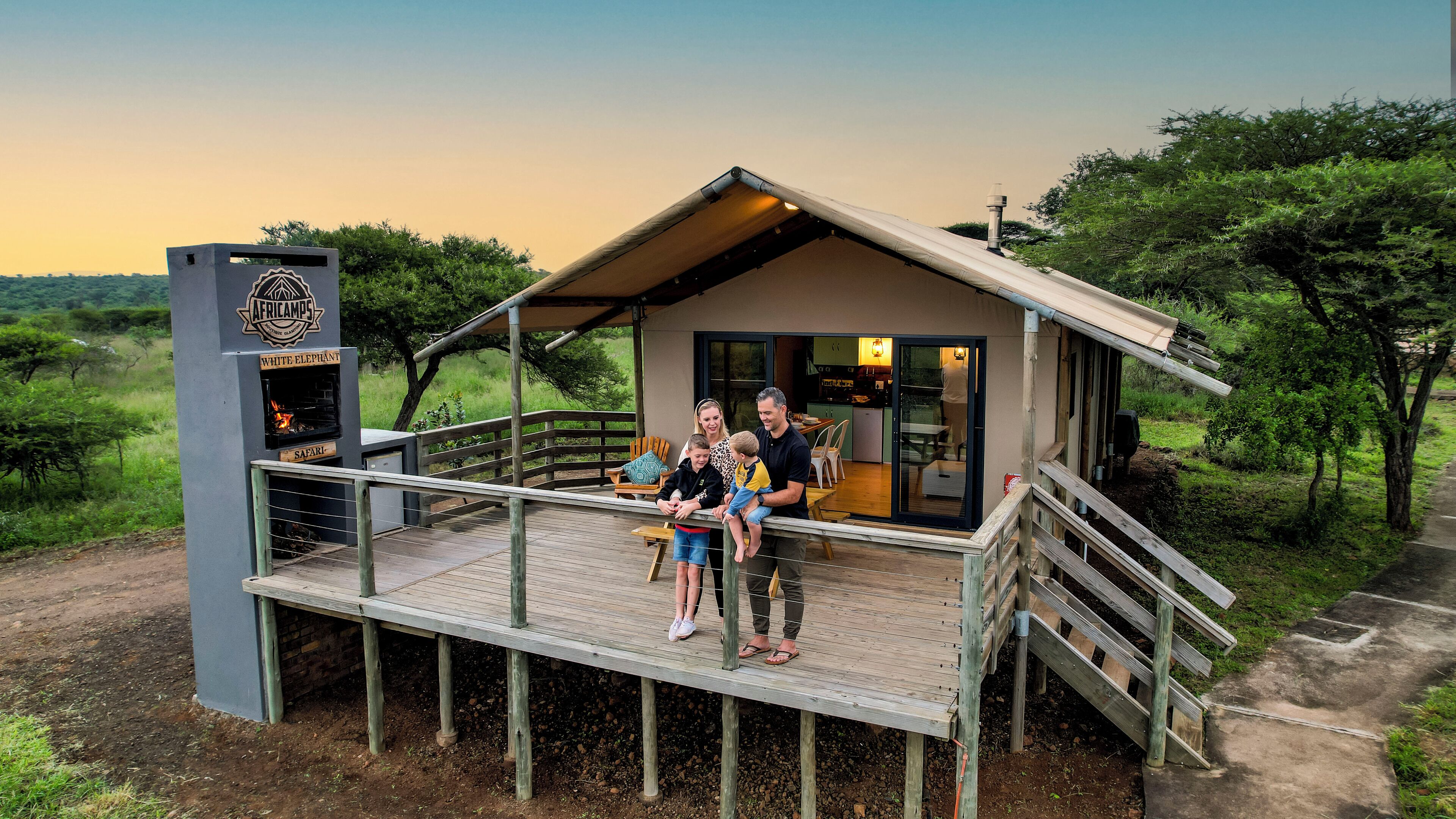 A family on a wooden deck in front of a safari lodge with a view of the surrounding landscape.