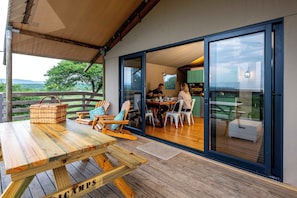 Een buiten eethoek met houten tafels en stoelen, een rieten mand en uitzicht op het landschap.
