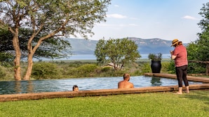 A pool with a view of mountains and a lake, surrounded by grass and trees.