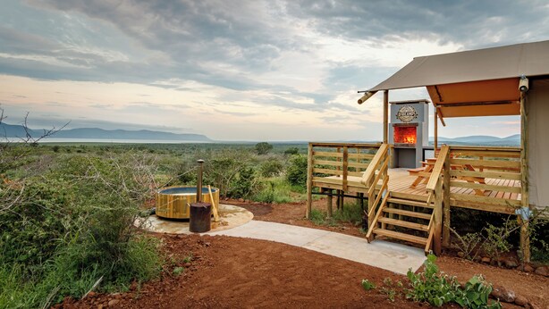 A wooden deck with a stone pathway leading to a tented area with a fireplace.