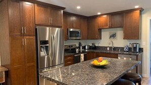 Uma cozinha moderna com armários de madeira, eletrodomésticos de aço inoxidável, bancada de granito e uma tigela de frutas.