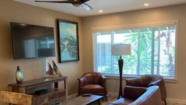 Uma sala de estar com sofá, cadeiras, mesa de centro, televisão e ventilador de teto.