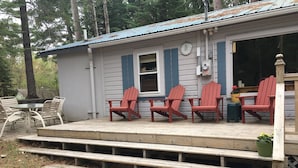 A wooden deck with four red Adirondack chairs and a table. - Cute, rustic cabin in Side Lake, No WiFi (Side Lake)