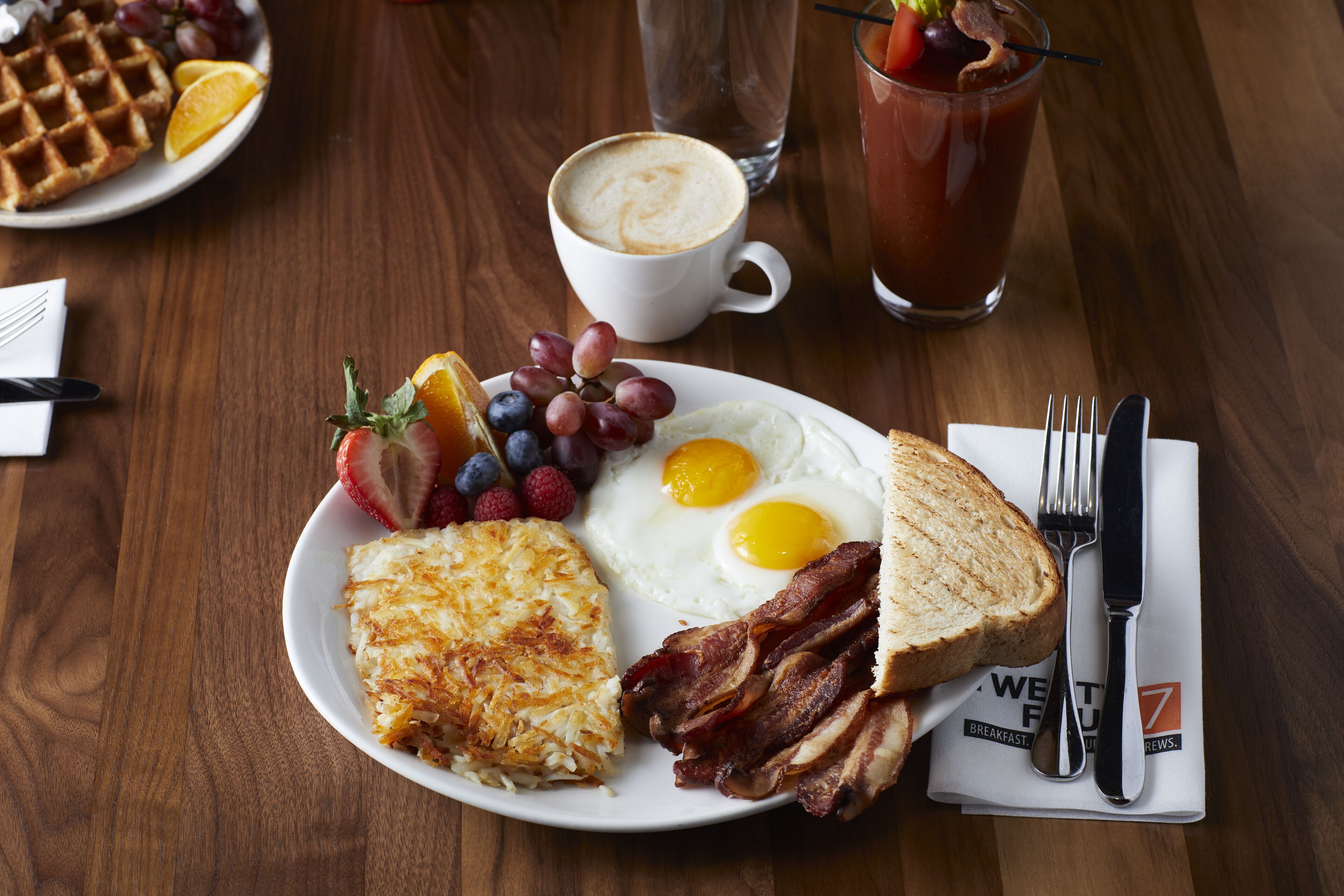 Un plato de desayuno con huevos, tocino, tostadas, patatas ralladas y fruta.