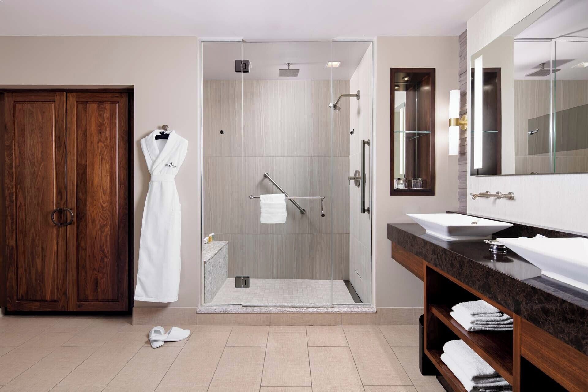 A modern bathroom with a glass-enclosed shower, a wooden wardrobe, a vanity with two sinks, and a large mirror.