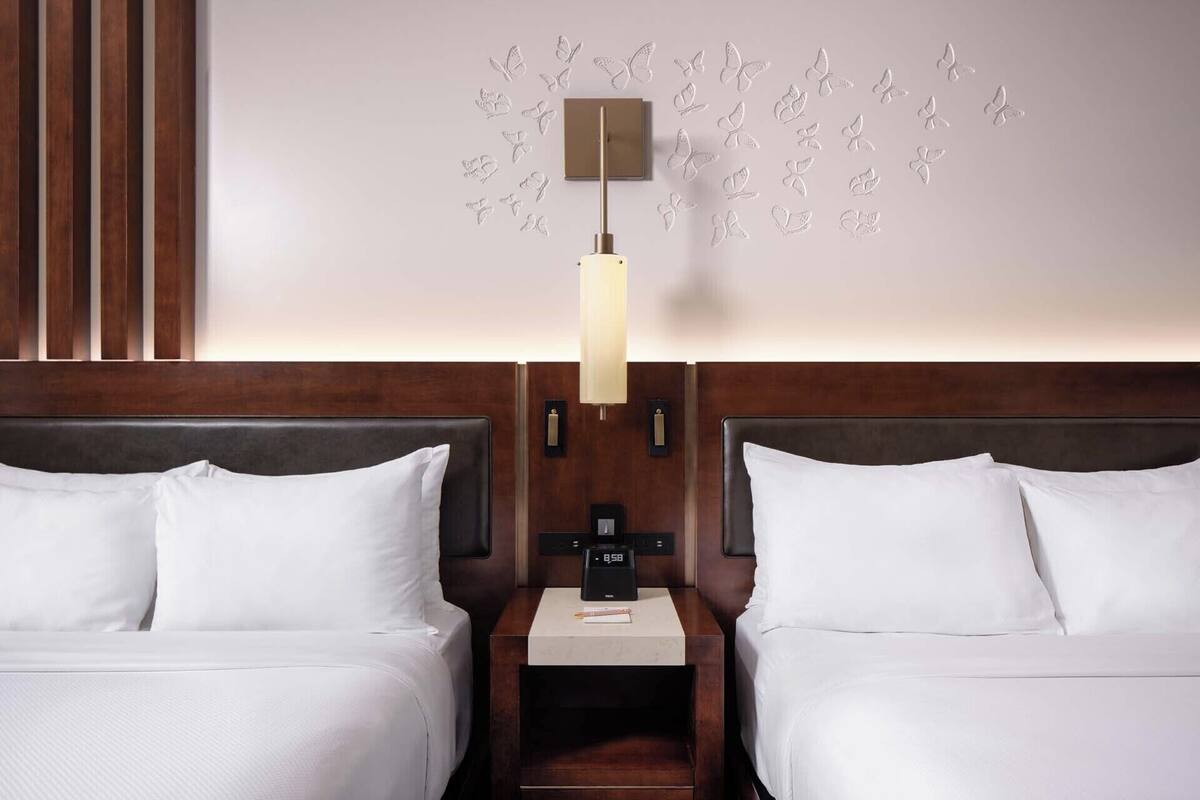 Une chambre d’hôtel avec deux lits, une table de chevet avec une horloge et un mur décoré de motifs de papillons.