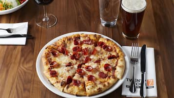 Una pizza con rodajas de pepperoni sobre un plato blanco, acompañada de una jarra de cerveza y un vaso de agua sobre una mesa de madera.