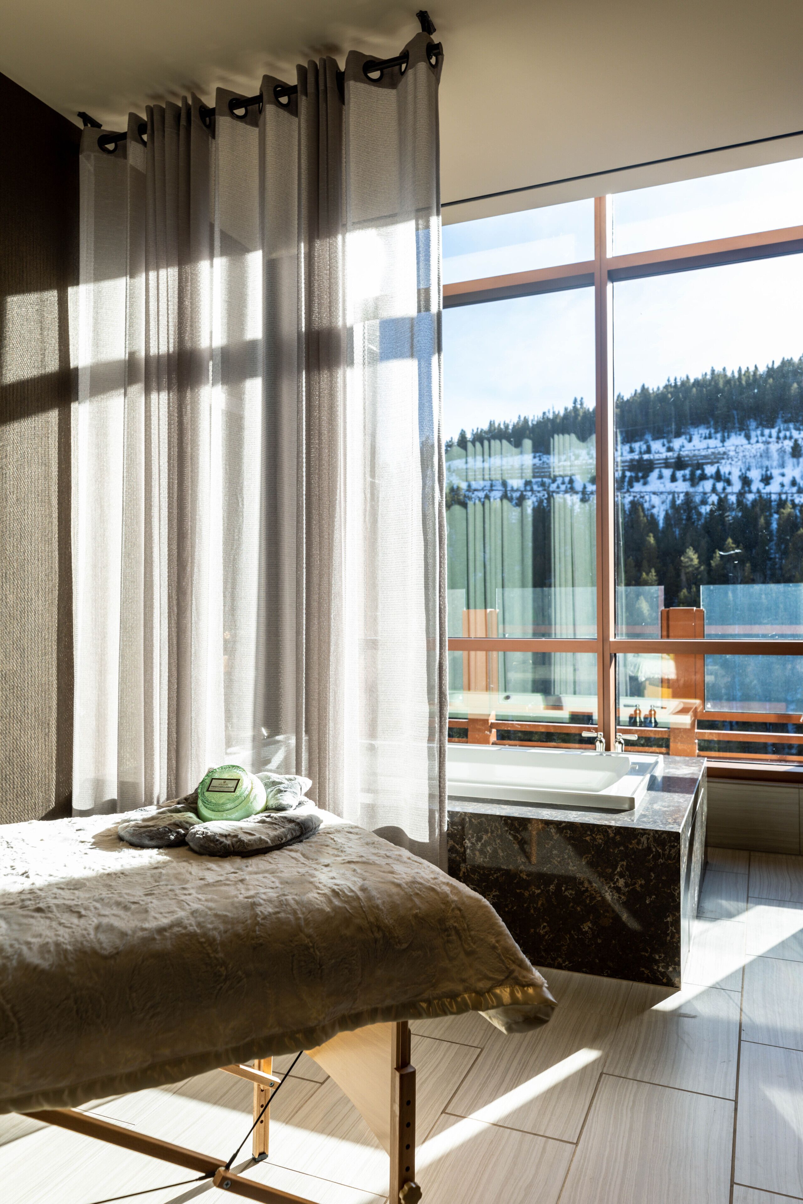 A bedroom with a large window, a bed, a wooden bench, and a view of a snowy landscape.