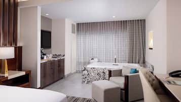 A hotel room with a bed, a desk, a chair, a small table, a sofa, a TV, and a bathroom with a bathtub and a shower.