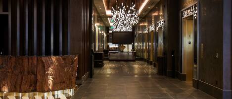 A modern hotel lobby with a reception desk, a large chandelier, and a reception area.