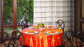Mesa de comedor preparada para seis personas, con manteles naranjas, sillas negras y vistas a zonas verdes a través de amplios ventanales.