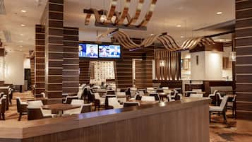 A modern hotel lobby with a reception desk, seating area, and a television displaying news.