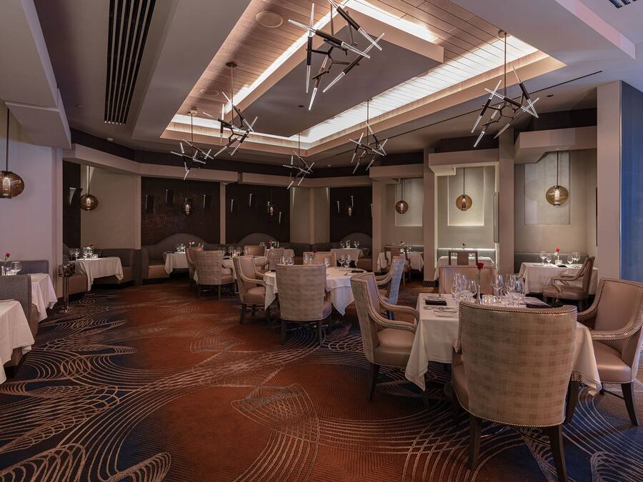 A spacious dining area with multiple tables and chairs, modern lighting fixtures, and a patterned carpet.
