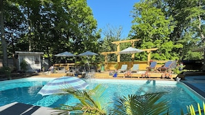 A swimming pool with lounge chairs and umbrellas, surrounded by trees and a wooden pergola. - ⚓Captain Bill's Guest House and heated pool access⚓ (Poland)