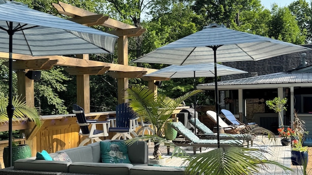 A covered outdoor seating area with wooden furniture and umbrellas, surrounded by lush greenery. - ⚓Captain Bill's Guest House and heated pool access⚓ (Poland)
