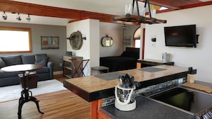 A modern kitchen with a large island, a dining table, and a black sofa in the living area. - ⚓Captain Bill's Guest House and heated pool access⚓ (Poland)