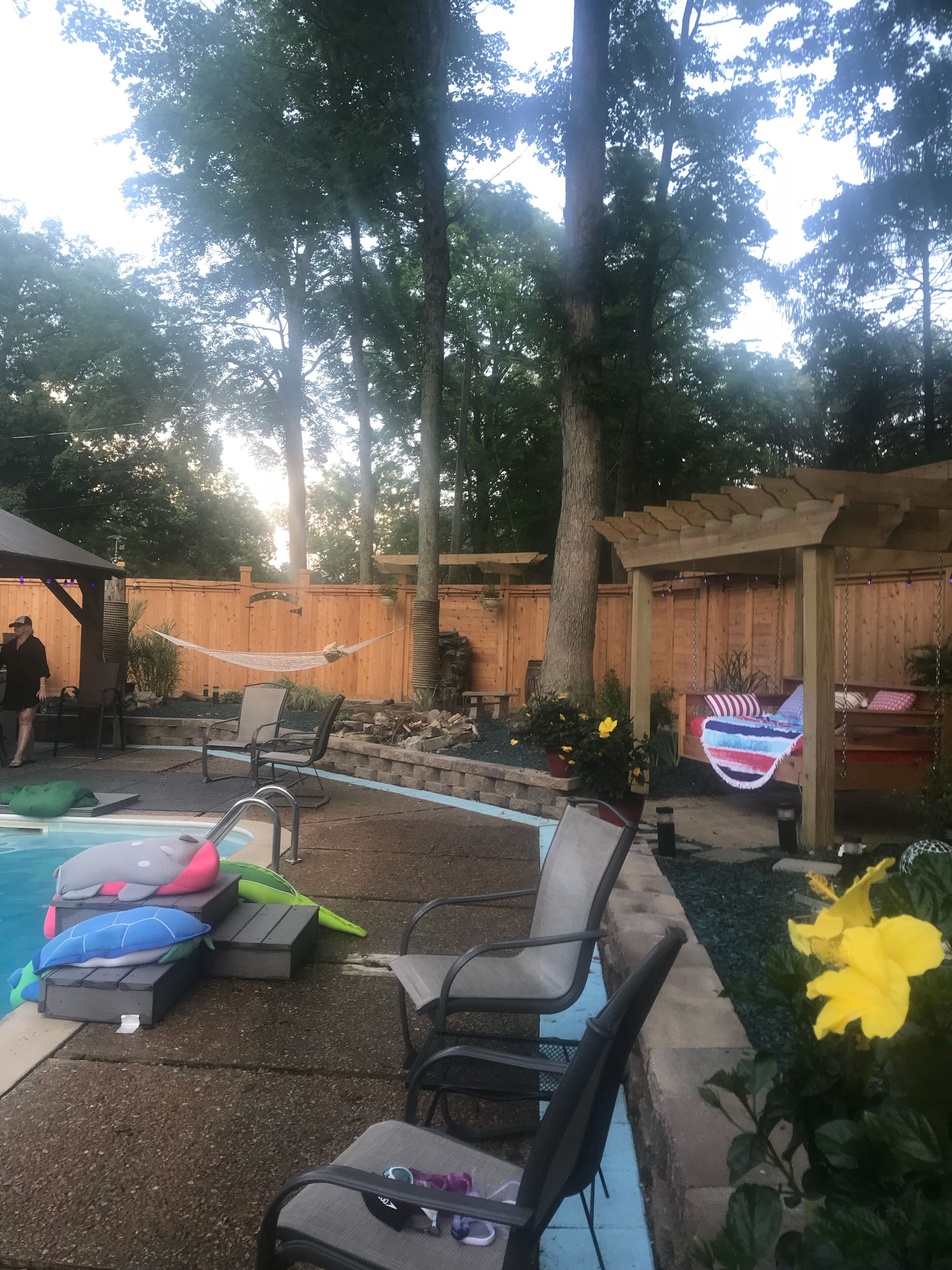 Un jardin avec une piscine, des chaises longues, un hamac et une pergola en bois.