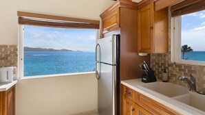 A kitchen with a view of the ocean, a refrigerator, wooden cabinets, and a sink. - Villa Anguillitta (Blowing Point)