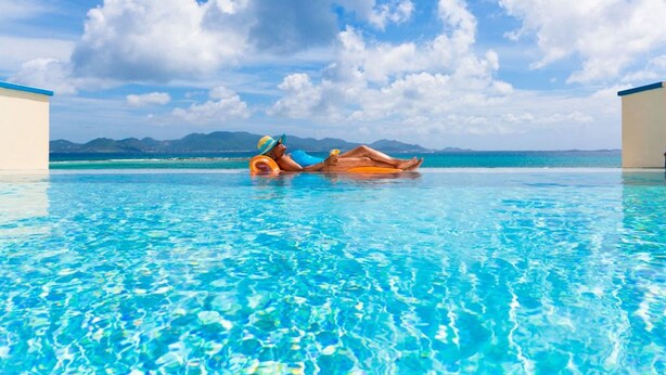 A clear blue pool with two people lying on floaties, surrounded by a clear sky and distant mountains. - Villa Anguillitta (Blowing Point)