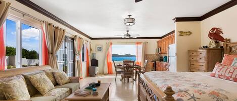 Een ruime kamer met een groot bed, een bank, een eettafel en uitzicht op zee.