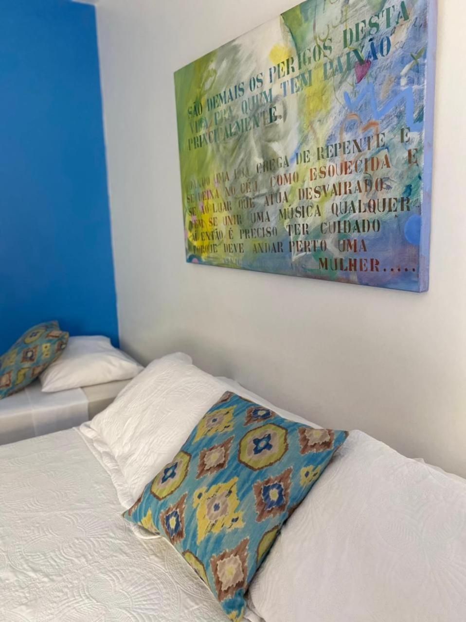 Una habitación con una cama, almohadas y un cuadro abstracto de colores en la pared.