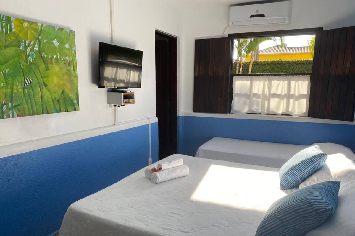 A hotel room with a bed, a TV, a window with curtains, and a painting on the wall.
