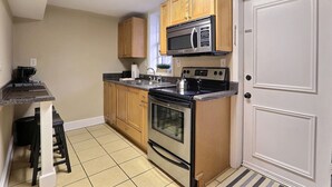 A compact kitchen with wooden cabinets, a microwave, a stove, and a sink. - Cozy Condo with Patio 1 Block to Forsyth Park (Savannah)