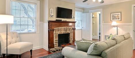 A living room with a fireplace, a sofa, a chair, a TV, and a ceiling fan.