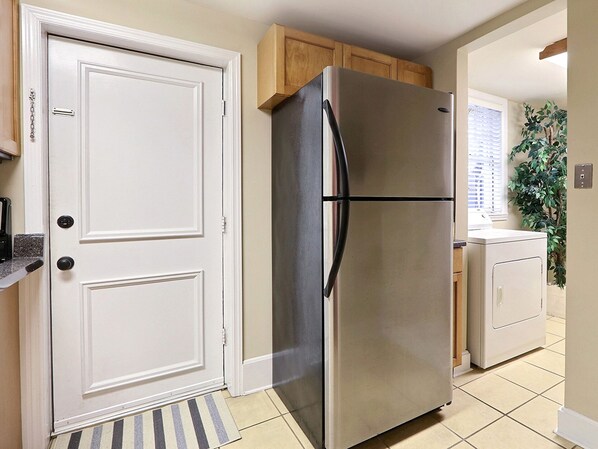 Una cucina con frigorifero in acciaio inossidabile, porta doppia, mobili in legno, lavatrice e un tappetino a righe.