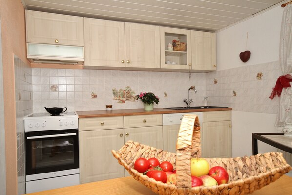A kitchen with white cabinets, a stove, a sink, and a basket of fruit on the counter.