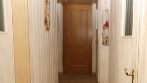 Un pasillo con suelo de madera, paredes blancas y una puerta de madera al final.
