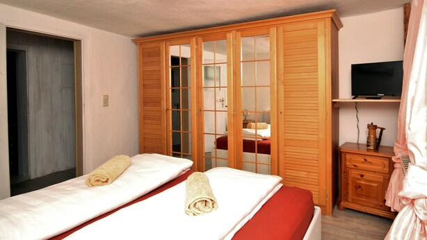 Habitación de hotel con dos camas, un armario, un televisor y una mesita de noche con lámpara.