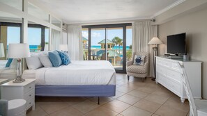 Une chambre d’hôtel avec un lit, une télévision, une chaise et vue sur la plage.