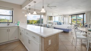 Une chambre d’hôtel moderne dotée d’un grand îlot central dans la cuisine, d’un coin repas séparé, d’un lit avec vue et d’un balcon offrant une vue sur la ville.